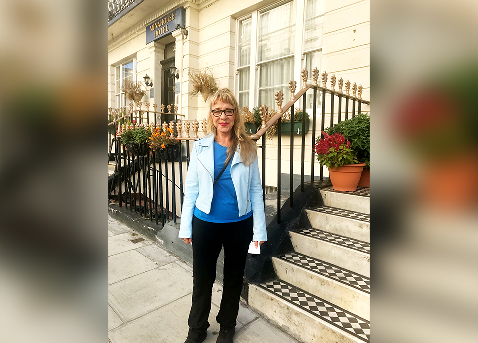 Woman with blonde hair and glasses standing on steps outside a building.